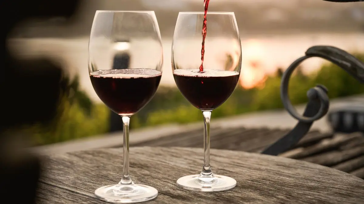 two glasses of red wine on a wooden table with the sea in the background
