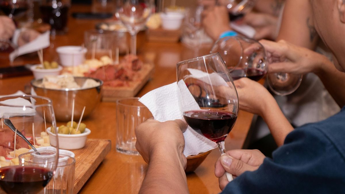 people at a wooden table checking the colour of red wine in wine glasses