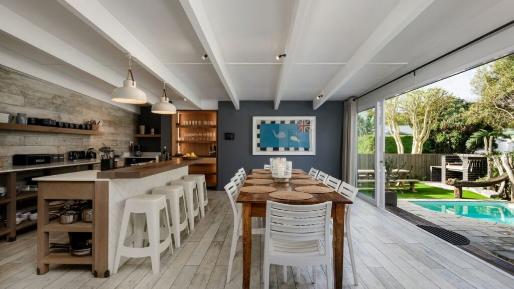 a large open plan living area with a long dining room table and doors opening to the outside patio and pool
