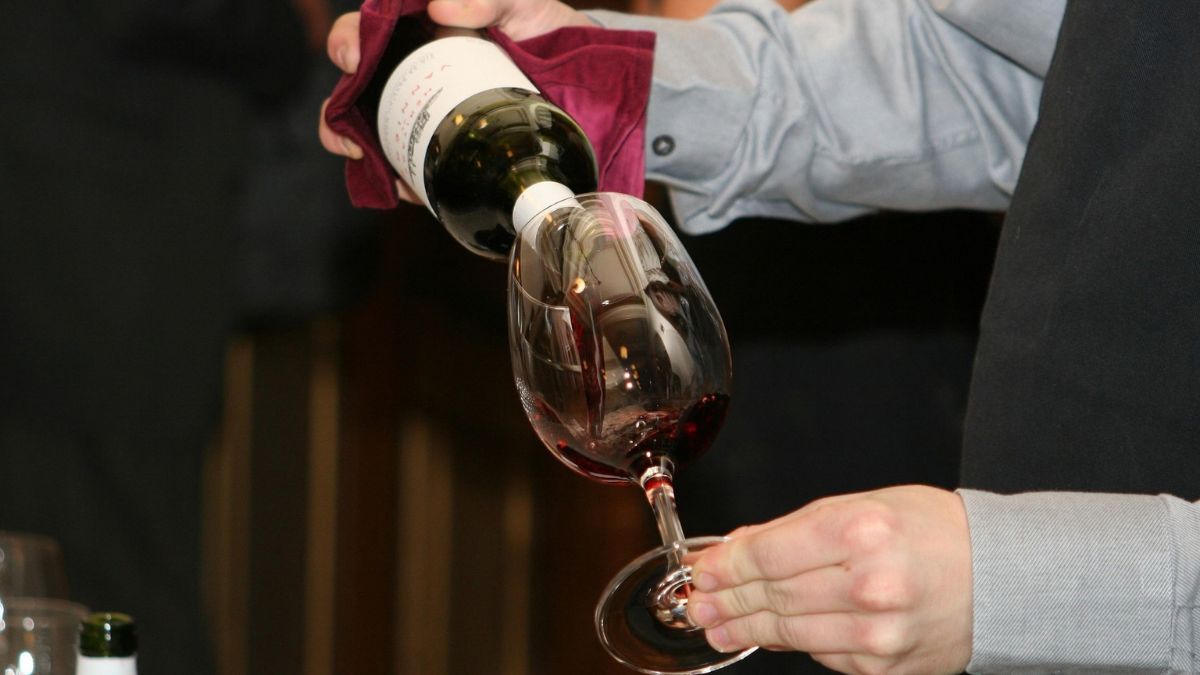 a waitron pouring red wine into a glass