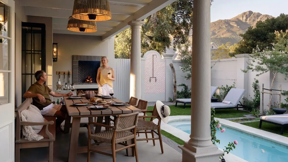 people relaxing on a patio next to a garden and swimming pool