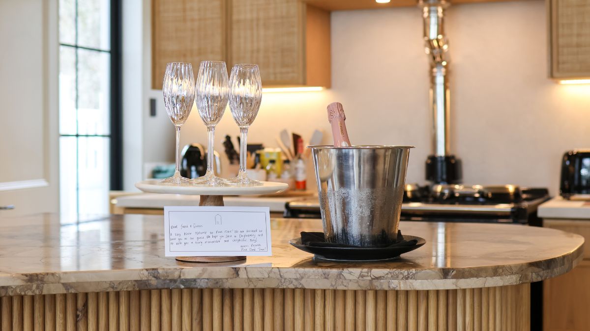 a bottle of sparkling wine in a wine cooler with three champagne flutes, on a marble kitchen counter