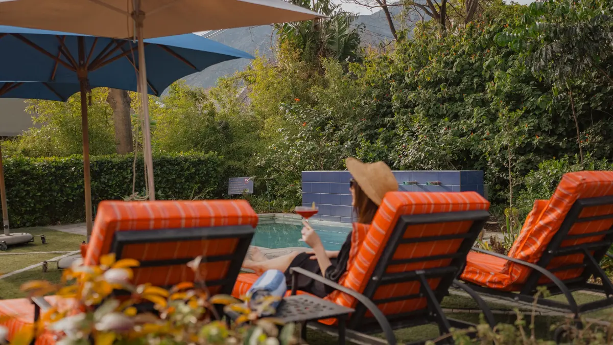 a woman wearing a hat sitting on a red relcliner alongside a pool